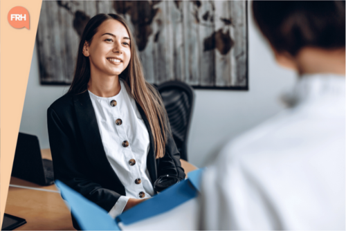 Jeune femme souriante en entretien de recrutement, assise face à un recruteur, dans un bureau professionnel.